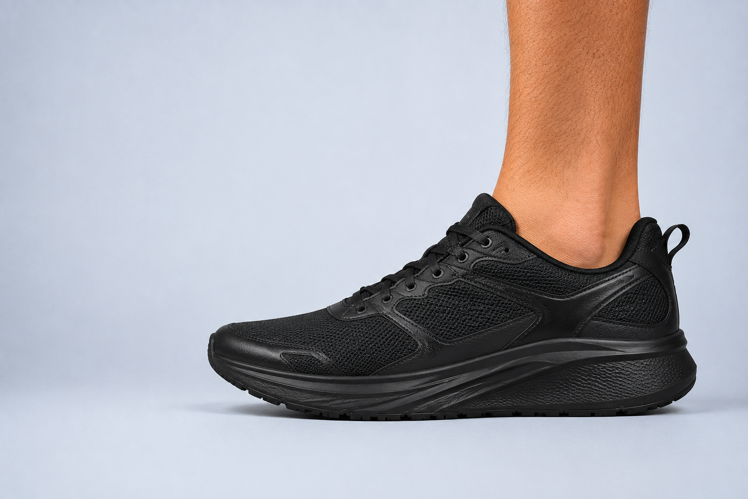 Black athletic trainer worn on a man's foot, shot at ground level against a pale blue-grey backdrop
